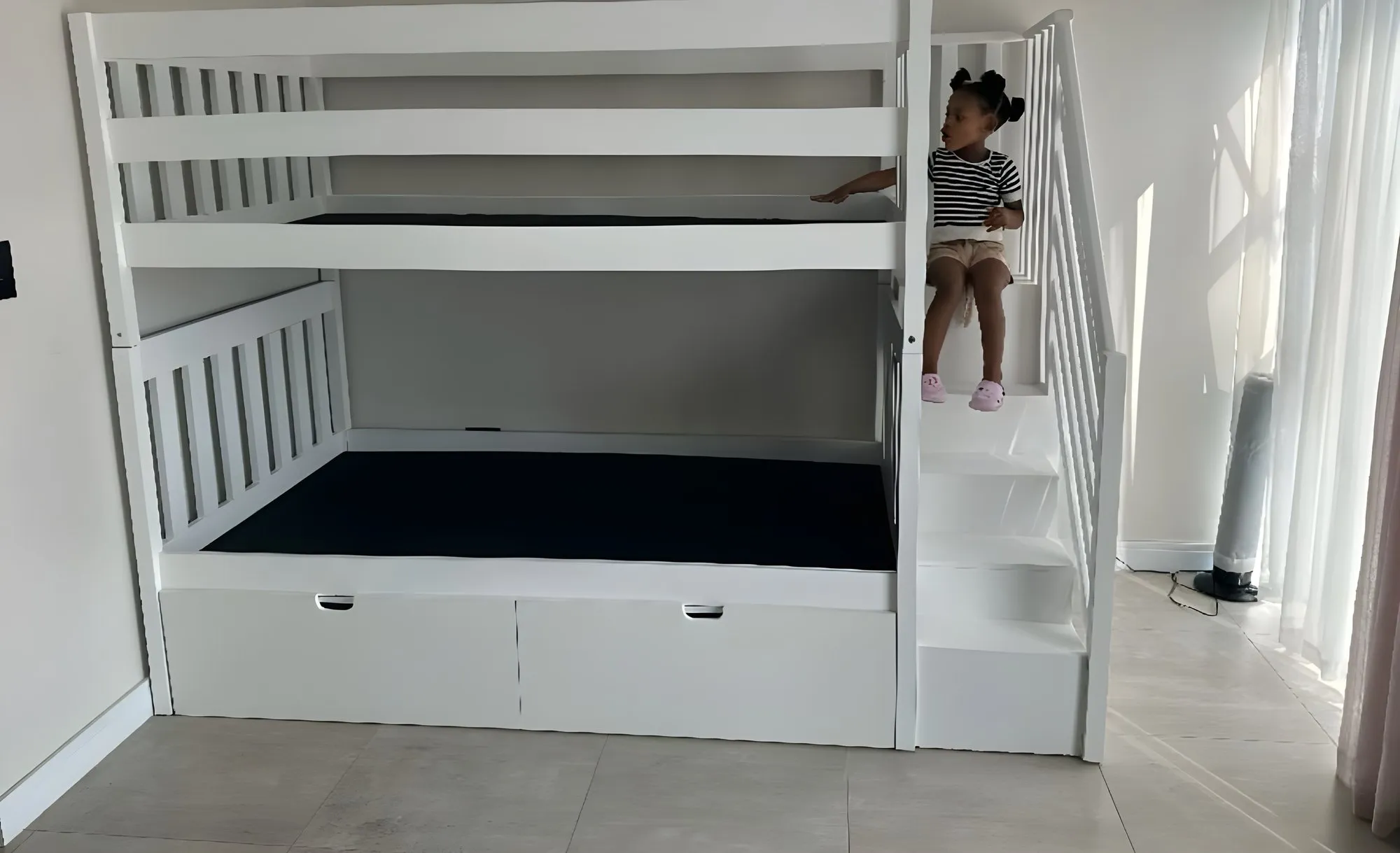 The same bunk bed painted white, with stairs and storage drawers, delivered to the room it was built for