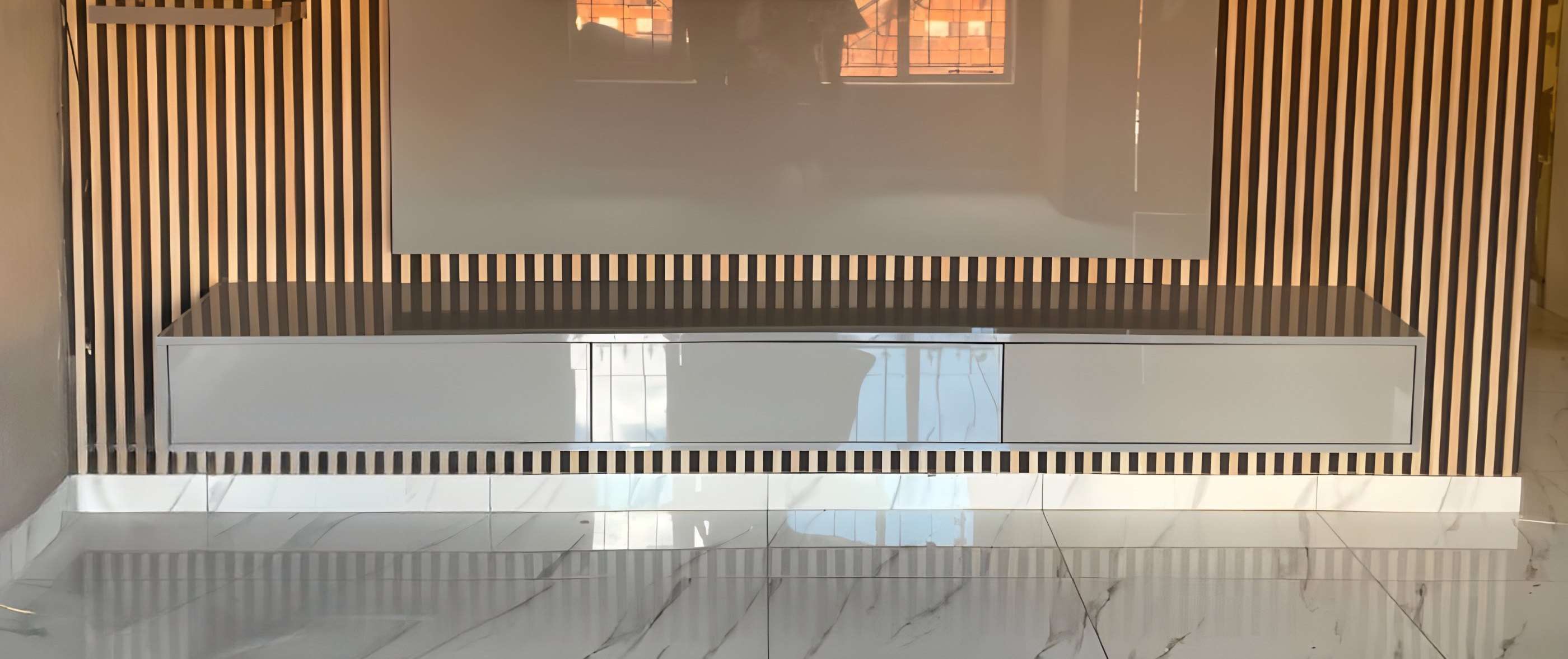 Wall-mounted TV on a slatted wood feature wall above a long white TV stand