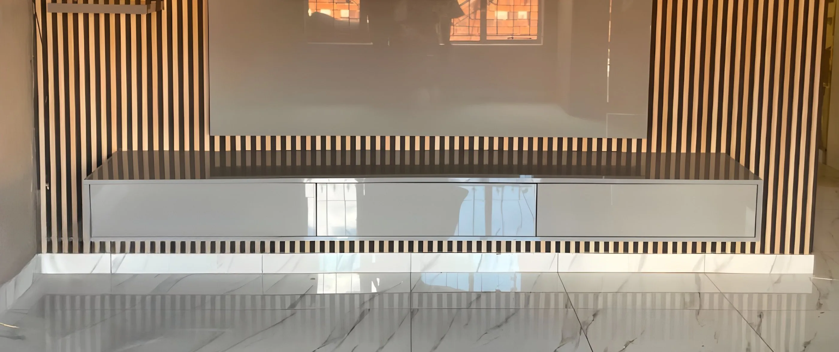Wall-mounted TV on a slatted wood feature wall above a long white TV stand