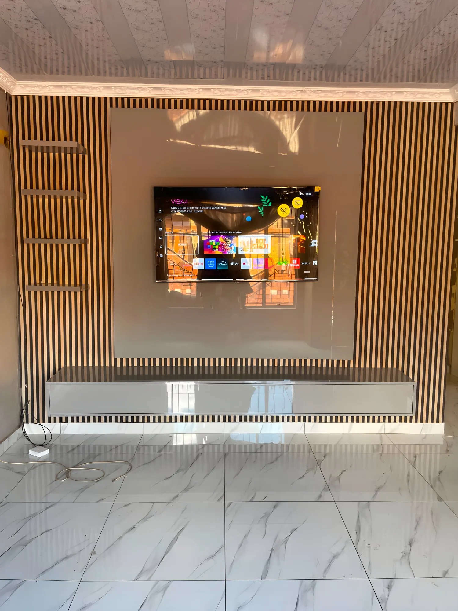 Wall-mounted TV on a slatted wood feature wall above a long white TV stand